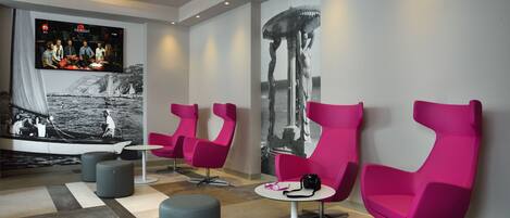 A modern lounge area with vibrant pink chairs, a flat-screen TV, and a large abstract painting.