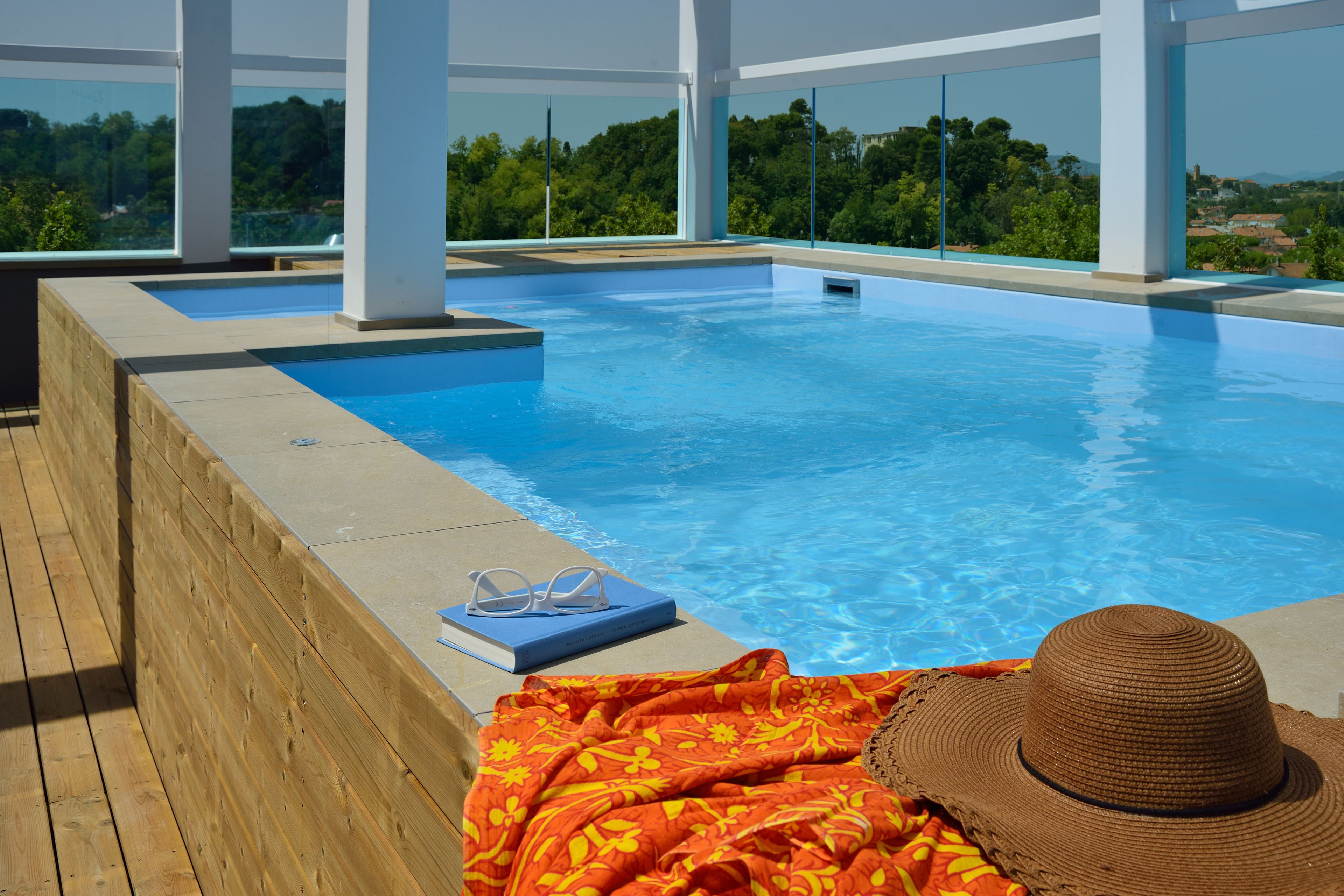 Une piscine à débordement située sur le toit, avec une terrasse en bois, une serviette bleue et un chapeau de paille.
