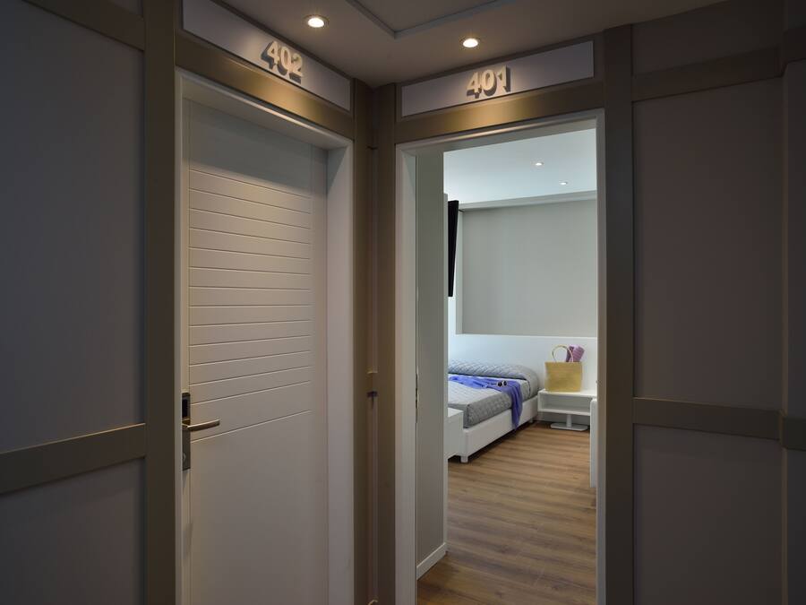 A hallway with doors labeled 402 and 401 leading to a bedroom with a bed, bedside table, and a nightstand.
