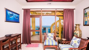 A room with a wooden chair, a small table, a decorative vase, and a painting on the wall. - Villa Del Playa Penthouse 5 (Roatan)