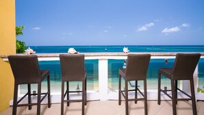 A balcony with four wicker chairs, a white railing, and a view of the ocean. - Villa Del Playa Penthouse 5 (Roatan)