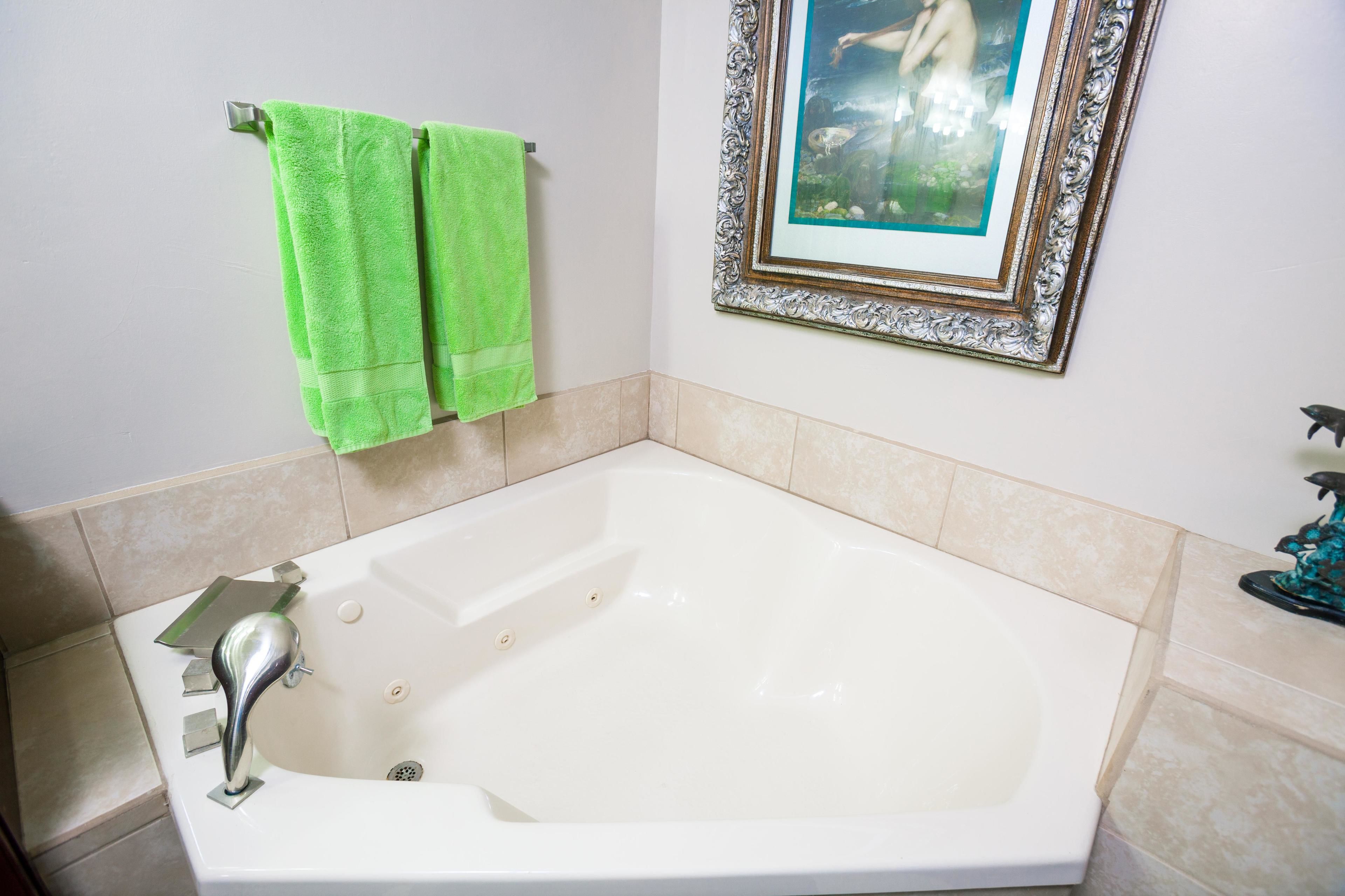 A bathroom with a large bathtub, two green towels, a framed picture on the wall, and a small statue on the side.