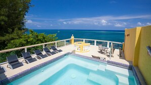 A pool with lounge chairs and a table, overlooking a clear blue sea with a sailboat in the distance. - Villa Del Playa Penthouse 5 (Roatan)