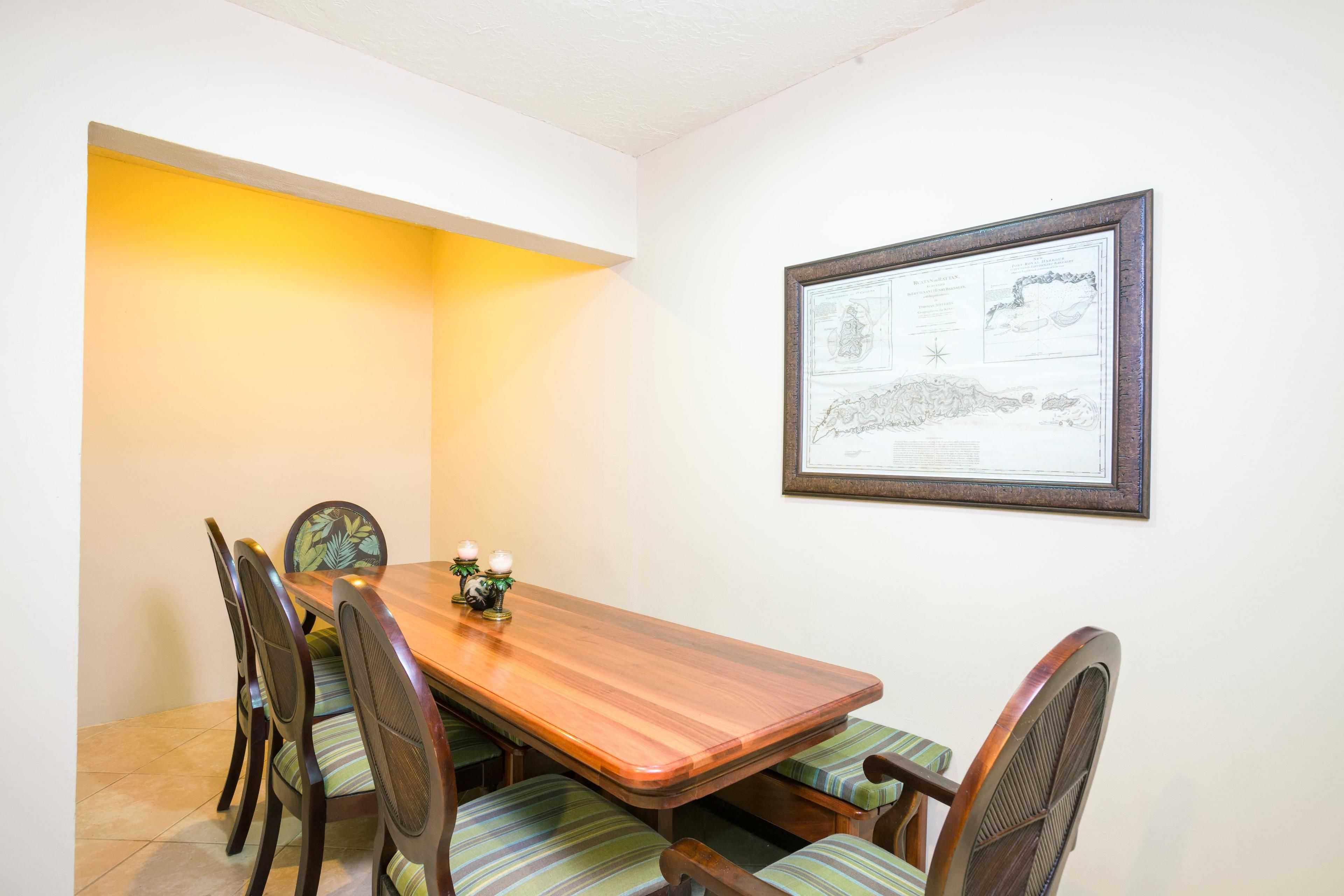 A dining area with a wooden table and chairs, a framed map on the wall, and a yellow wall accent.