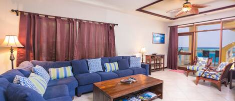 A living room with a blue sofa, wooden coffee table, and a view of the ocean through large windows.