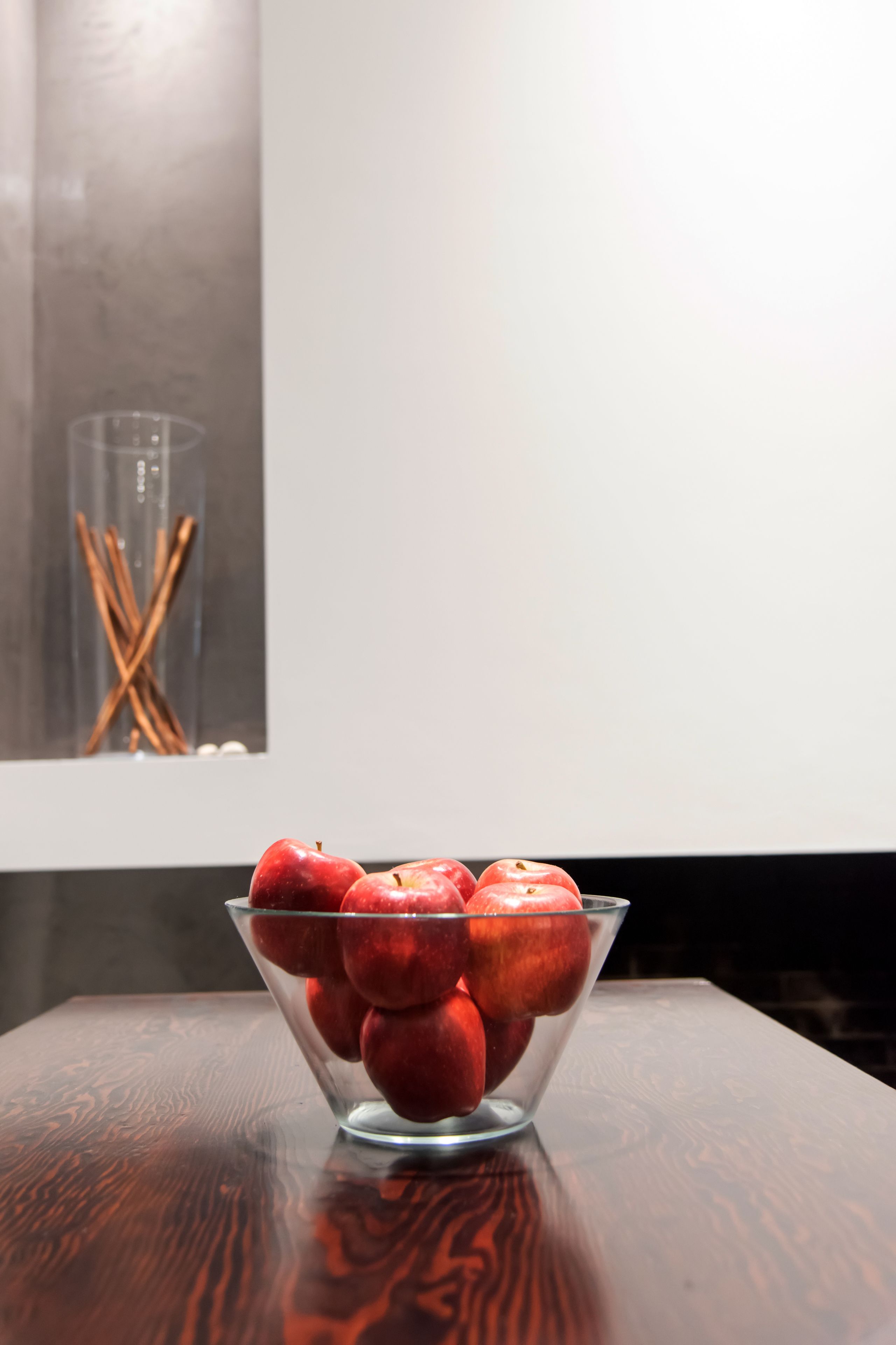 Un saladier en verre transparent rempli de pommes rouges, posé sur une table en bois.