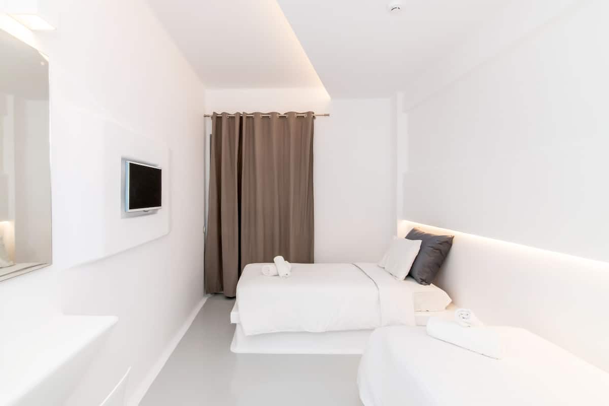 A modern hotel room with a bed, a sofa, a TV mounted on the wall, and a window with curtains.