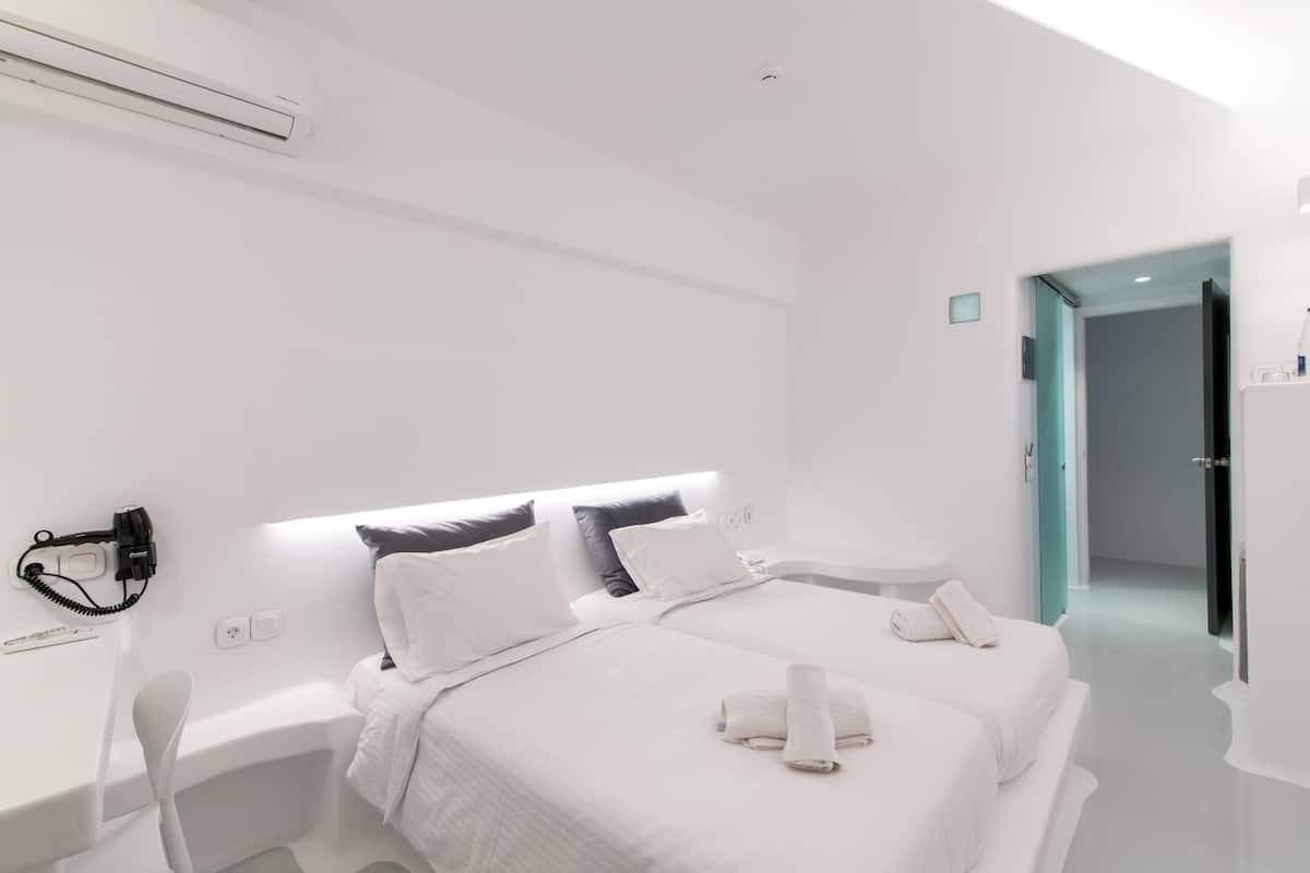A modern hotel room with two beds, a bedside table, a chair, and a bathroom door.