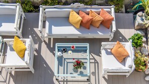 Een dakterras met twee witte lounge fauteuils, een glazen tafel met een bloemstuk en een potplant.