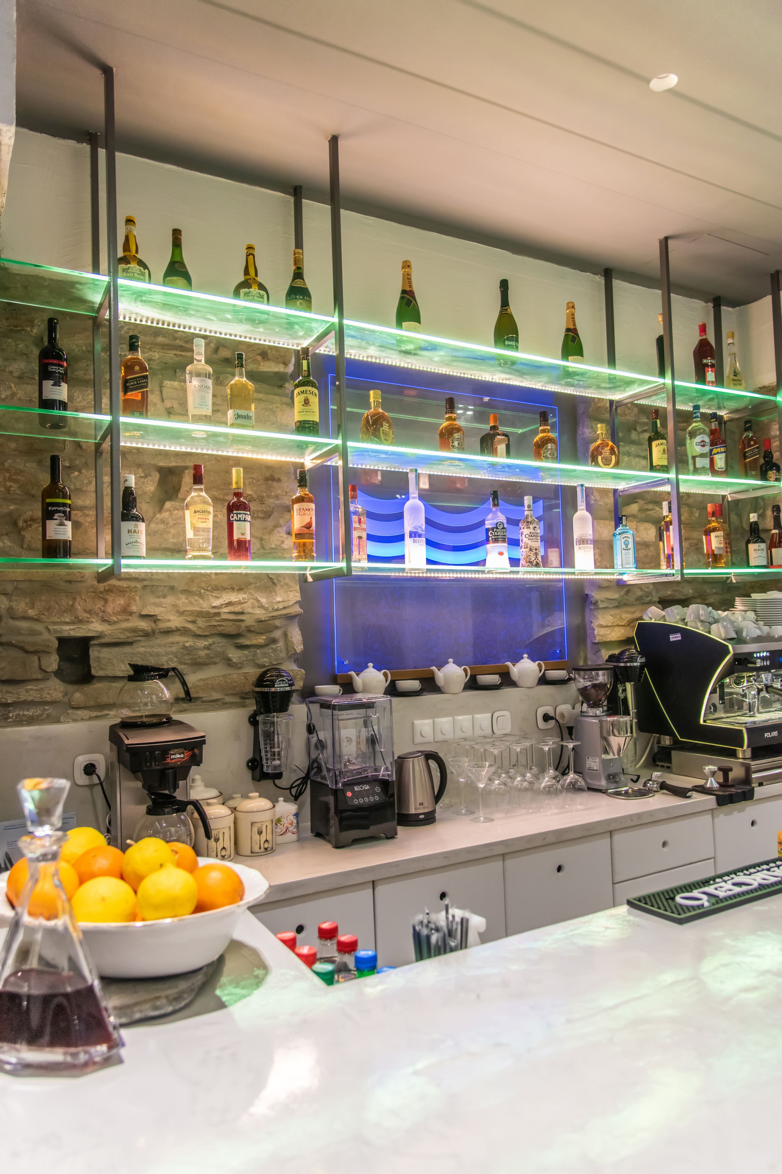 Una zona de bar con estantes llenos de botellas de licores, una cafetera y un bol de limones.