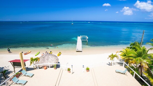 A beach with a pier, lounge chairs, and a thatched-roof structure. - Villa Del Playa Penthouse 6 (Roatan)