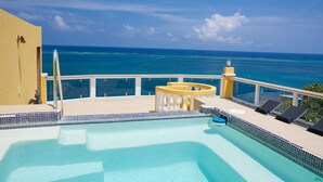 A pool with a view of the ocean, a yellow building, and a railing. - Villa Del Playa Penthouse 6 (Roatan)