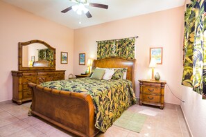 A bedroom with a wooden bed, a nightstand, a dresser, a ceiling fan, and a large mirror. - Villa Tranquila (Roatan)