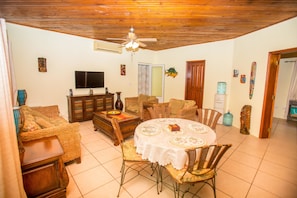 A living room with a dining table, wicker furniture, a flat-screen TV, and a ceiling fan.
