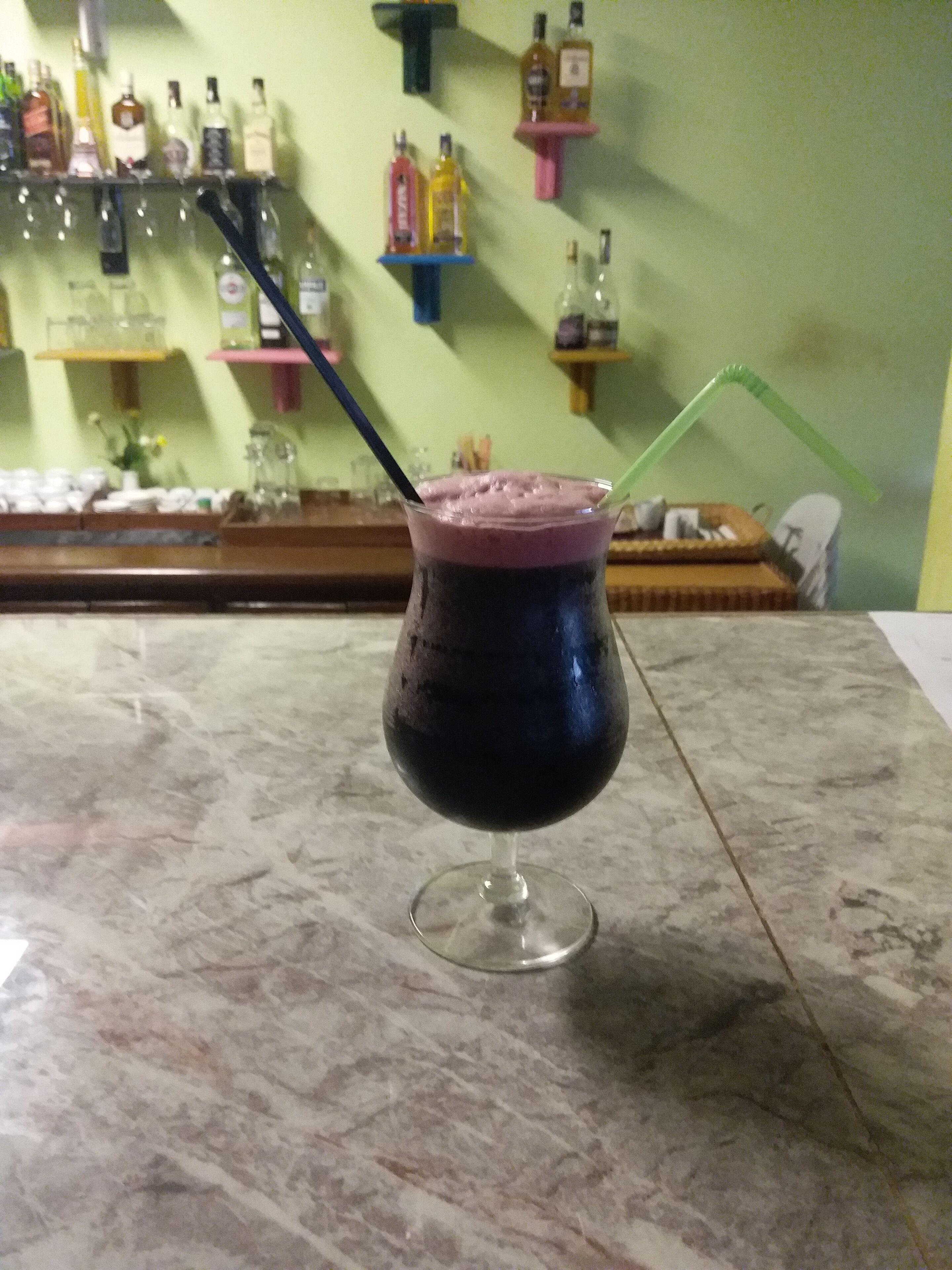 Um cocktail num copo com canudo sobre um balcão de mármore.