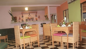 A checkered floor, wicker chairs with cushions, a bar area with bottles, and a green wall. - Liza Hôtel (Yaoundé)