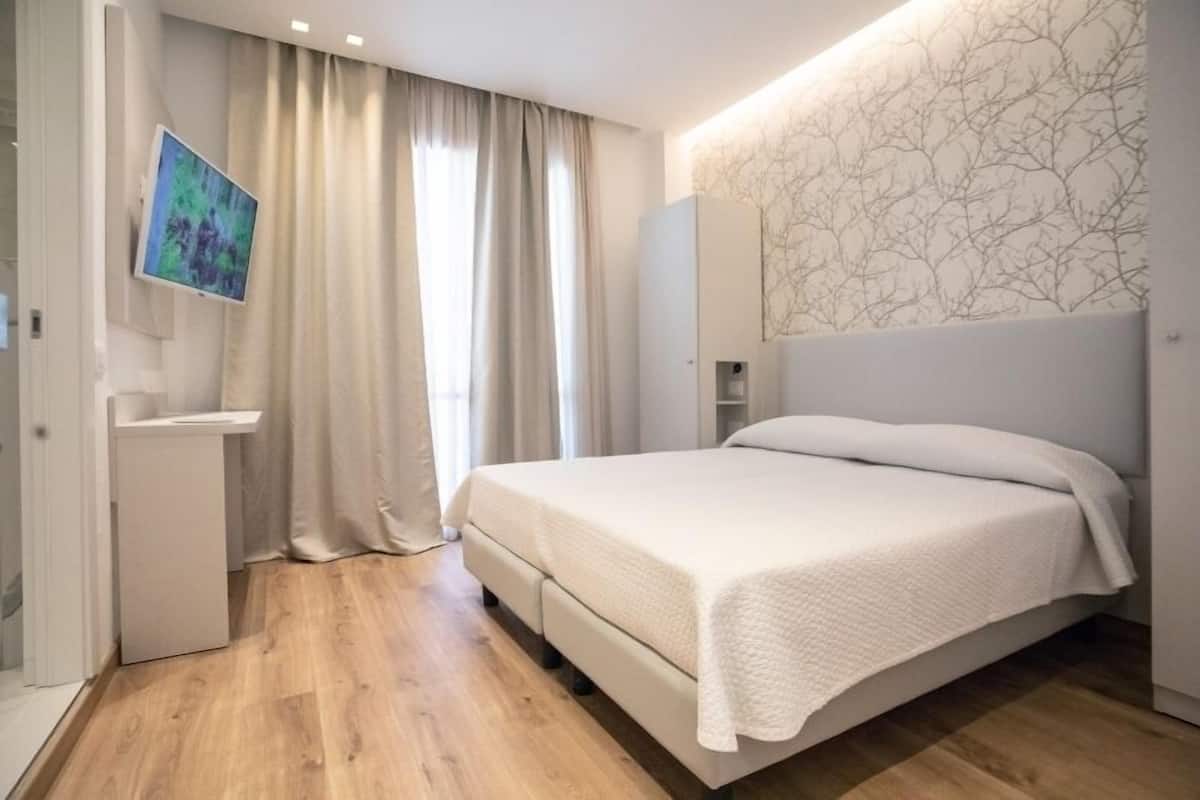 A modern bedroom with a bed, a flat-screen TV, a wardrobe, and a window with curtains.
