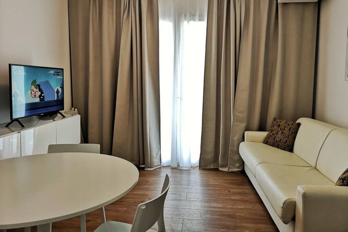 A living room with a television, a round table, a sofa, and curtains.