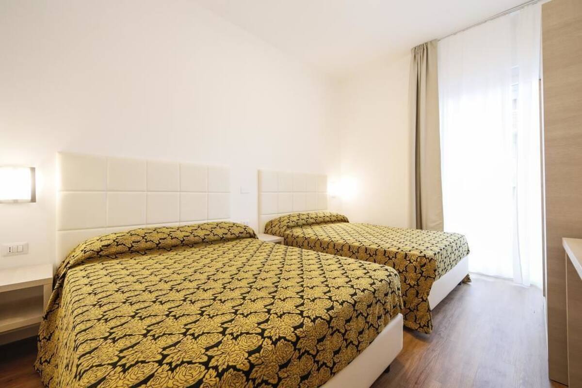 A hotel room with two beds, a large window with curtains, and a white headboard.