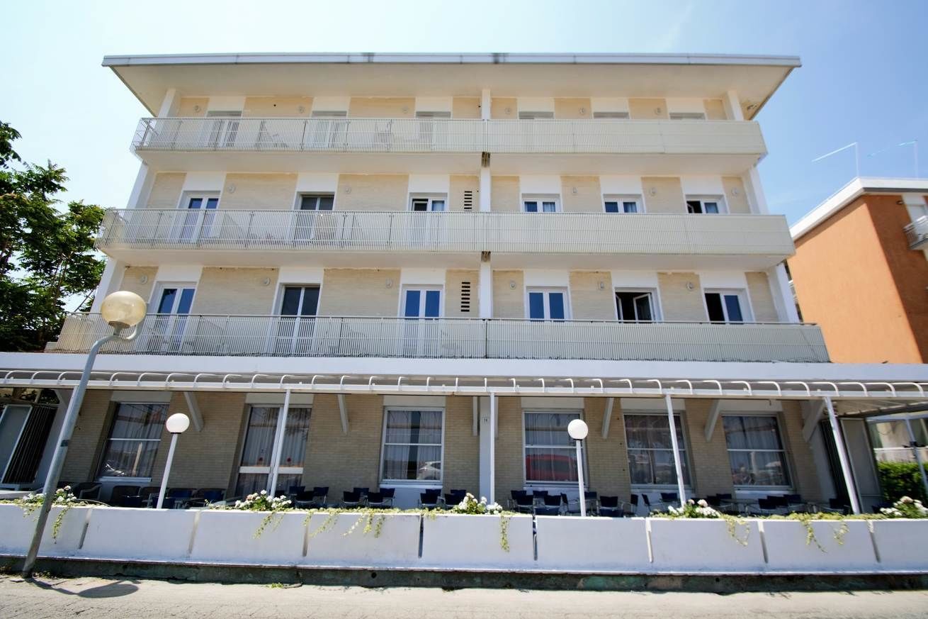 A multi-story building with balconies, a covered outdoor seating area, and a row of windows.