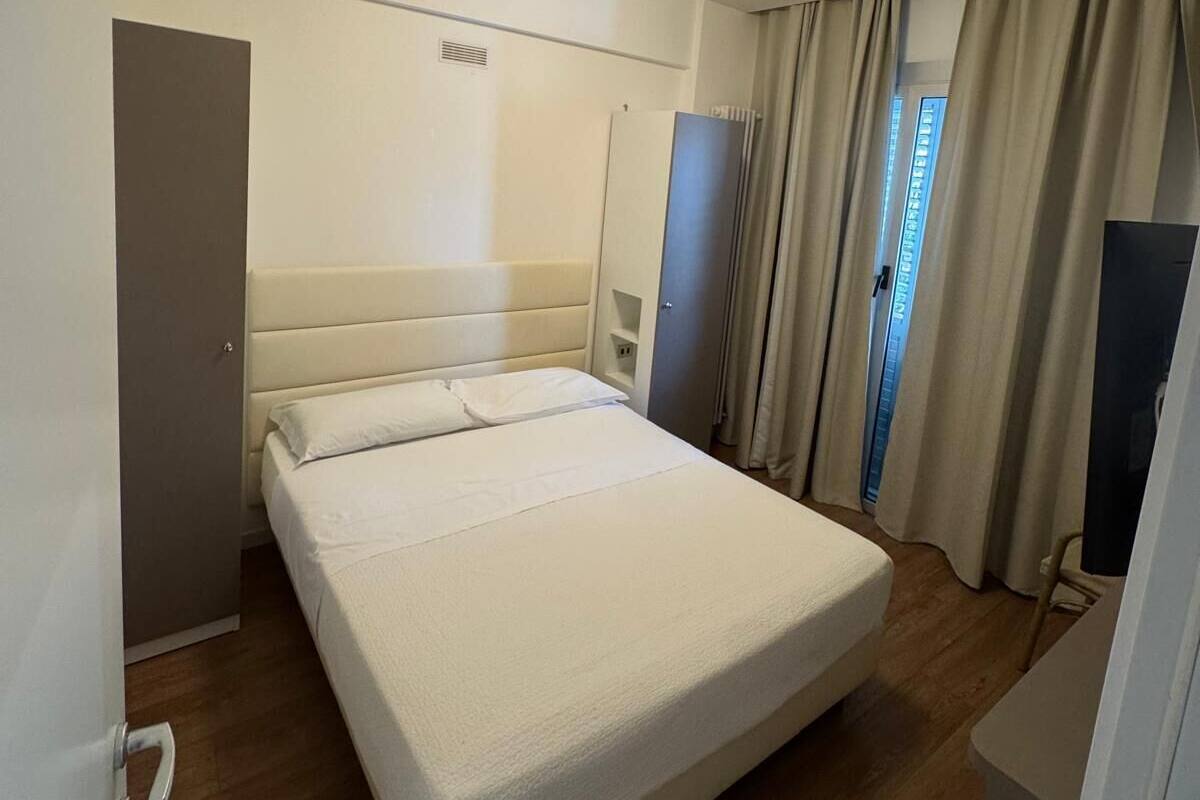 A hotel room with a large bed, a wardrobe, a mirror, and a ceiling light.