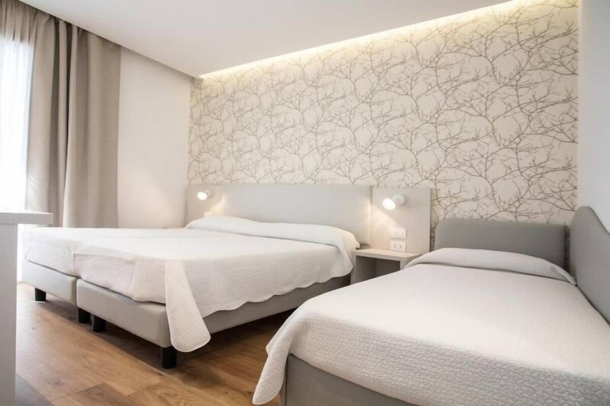 A hotel room with two beds, a nightstand, and a wall with a tree pattern.
