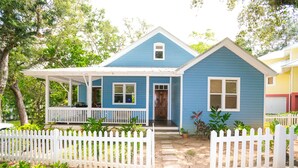 Uma casa de dois andares com fachada azul, varanda branca e cerca branca de piquete.
