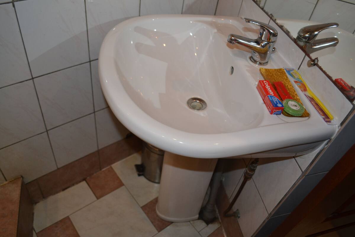 A bathroom sink with a white basin, chrome faucets, and a drain. There are toiletries on the sink's edge.