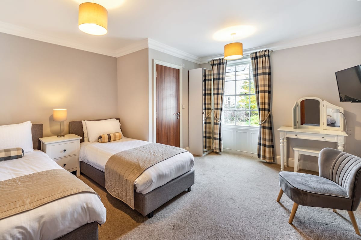 A hotel room with two beds, a desk, and a chair. There is a window with curtains and a television on the wall.