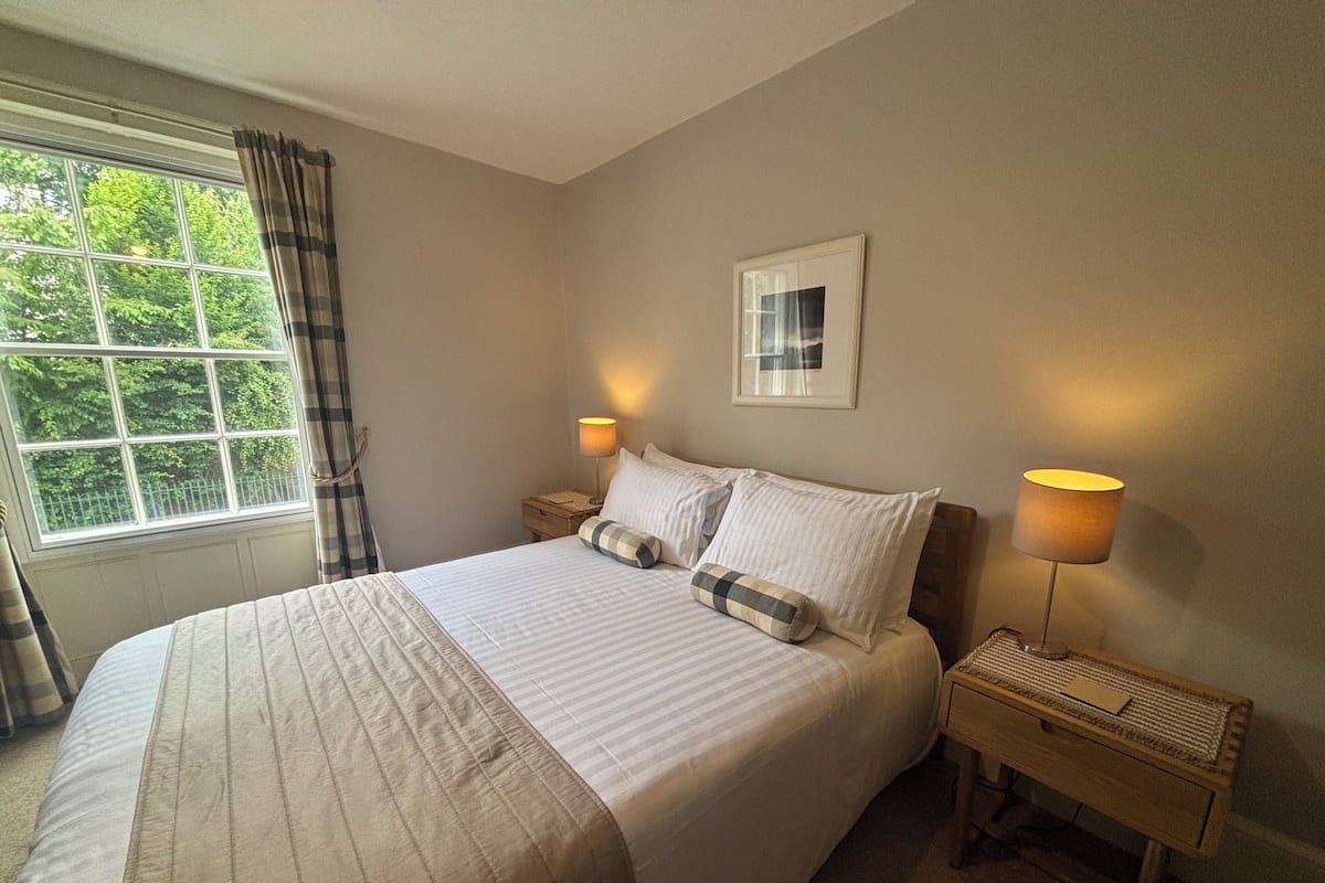 A neatly made bed with pillows, a bedside lamp, and a window with curtains.