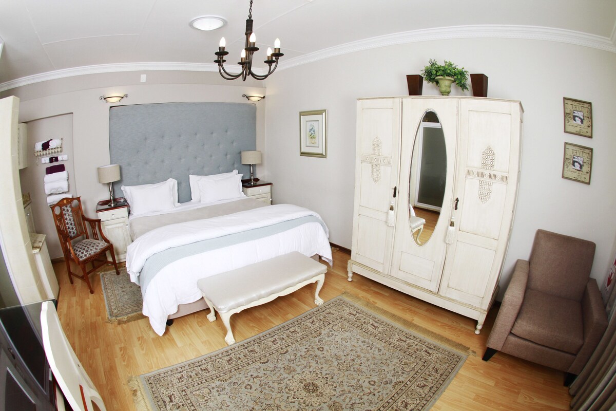A bedroom with a large bed, a wardrobe, a bench, a chair, and a chandelier.