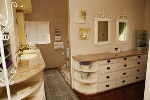A bathroom with two sinks, a vanity with drawers, a mirror, and a window with blinds. - Oleander Guest House (Kimberley)