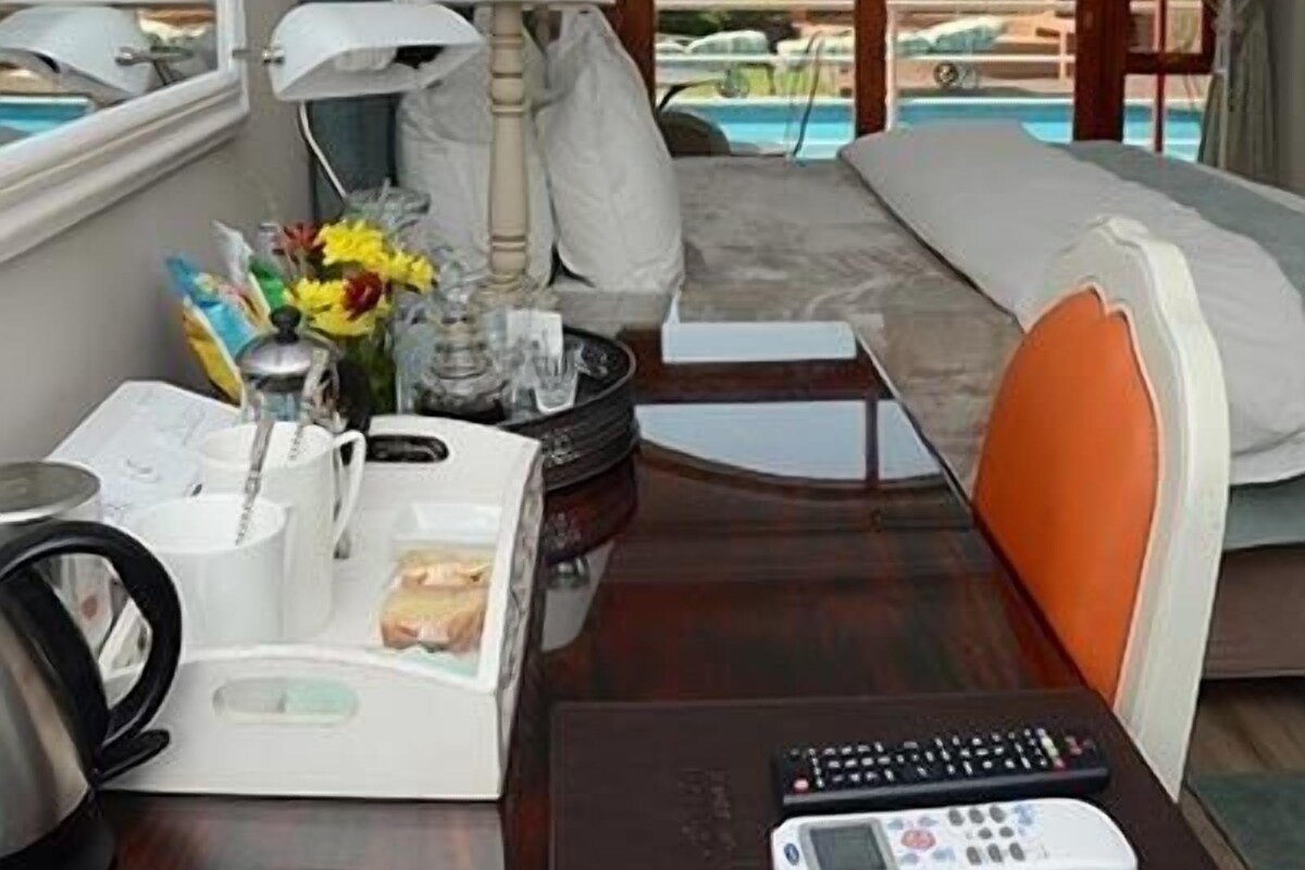 A hotel room with a bed, a desk with a lamp, a remote control, and a view of a pool.