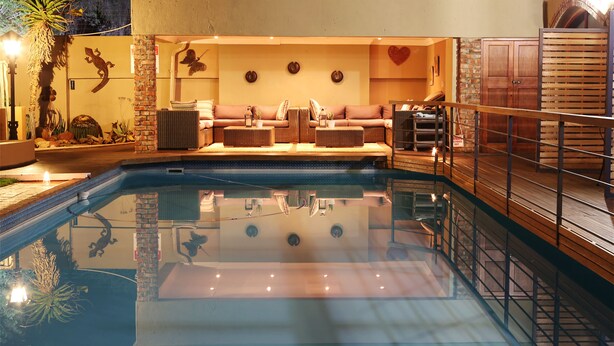 A pool area with a seating area, a brick wall, and a wooden deck. - Oleander Guest House (Kimberley)
