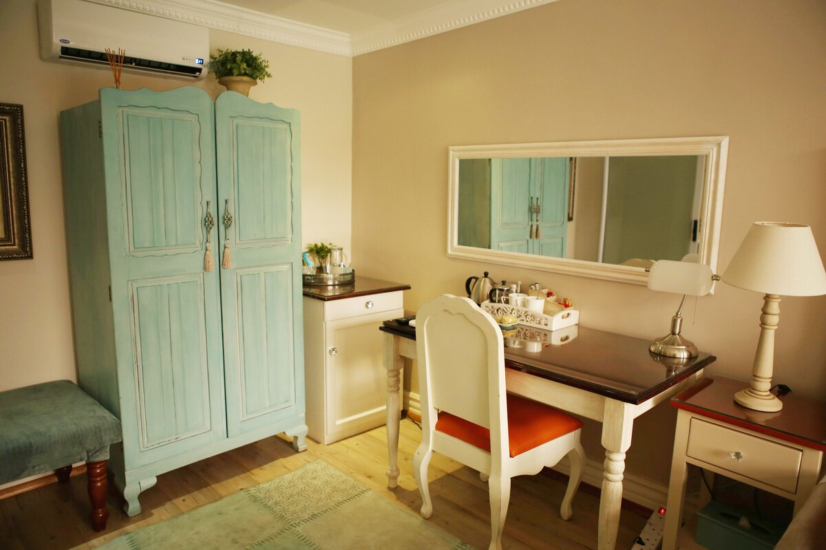 A room with a wooden desk, a white chair, a blue wardrobe, a mirror, and a lamp.