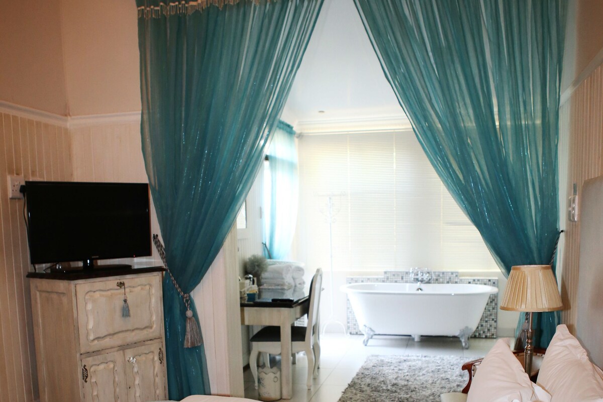 A bedroom with a bed, a dresser, a television, and a bathroom in the background.