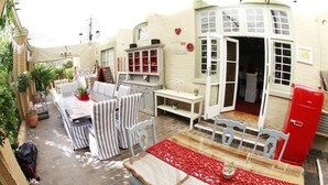 A cozy outdoor seating area with a table and chairs, surrounded by potted plants and a red refrigerator. - Oleander Guest House (Kimberley)
