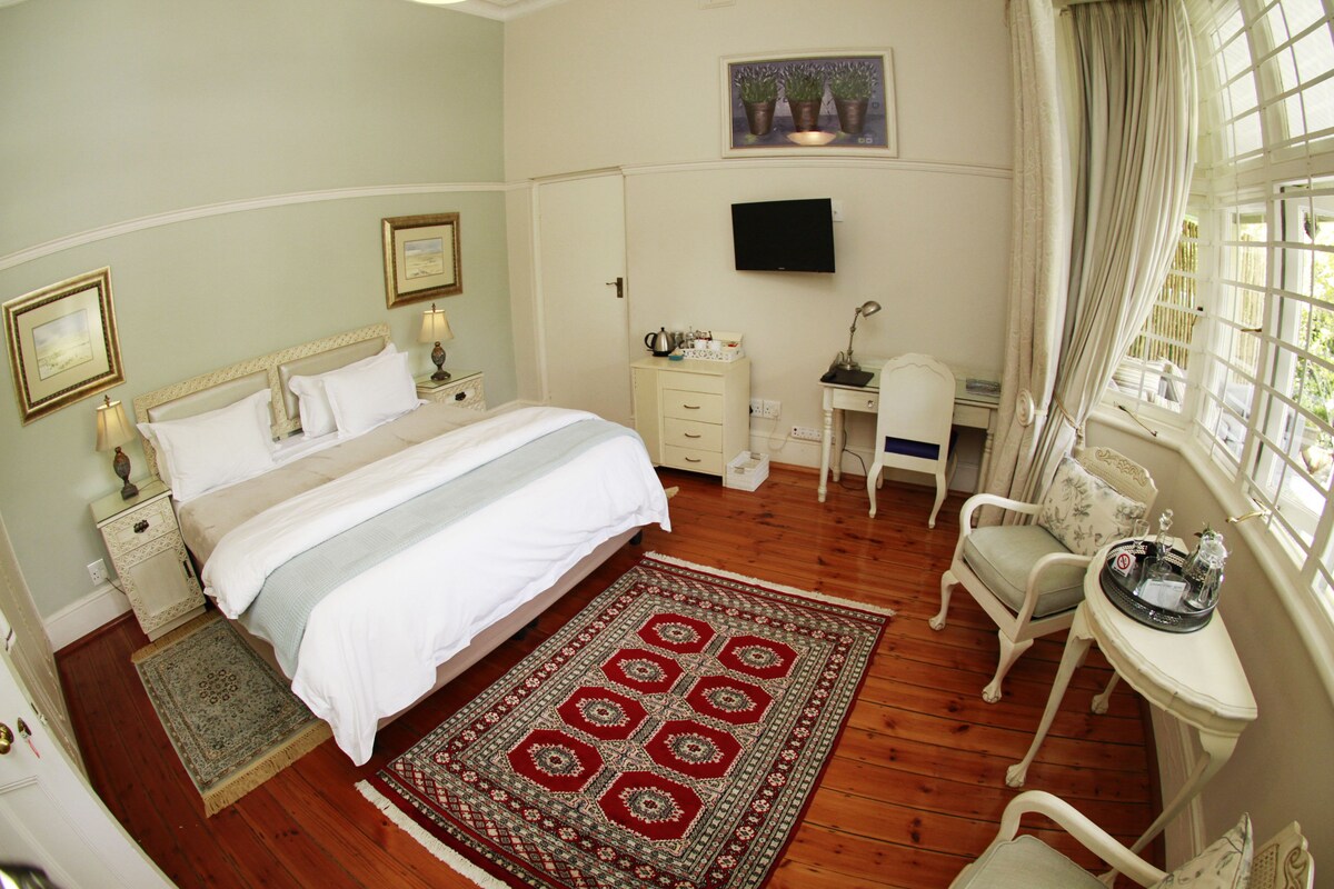 A bedroom with a bed, bedside tables, a desk, a chair, a TV, and a window with curtains.