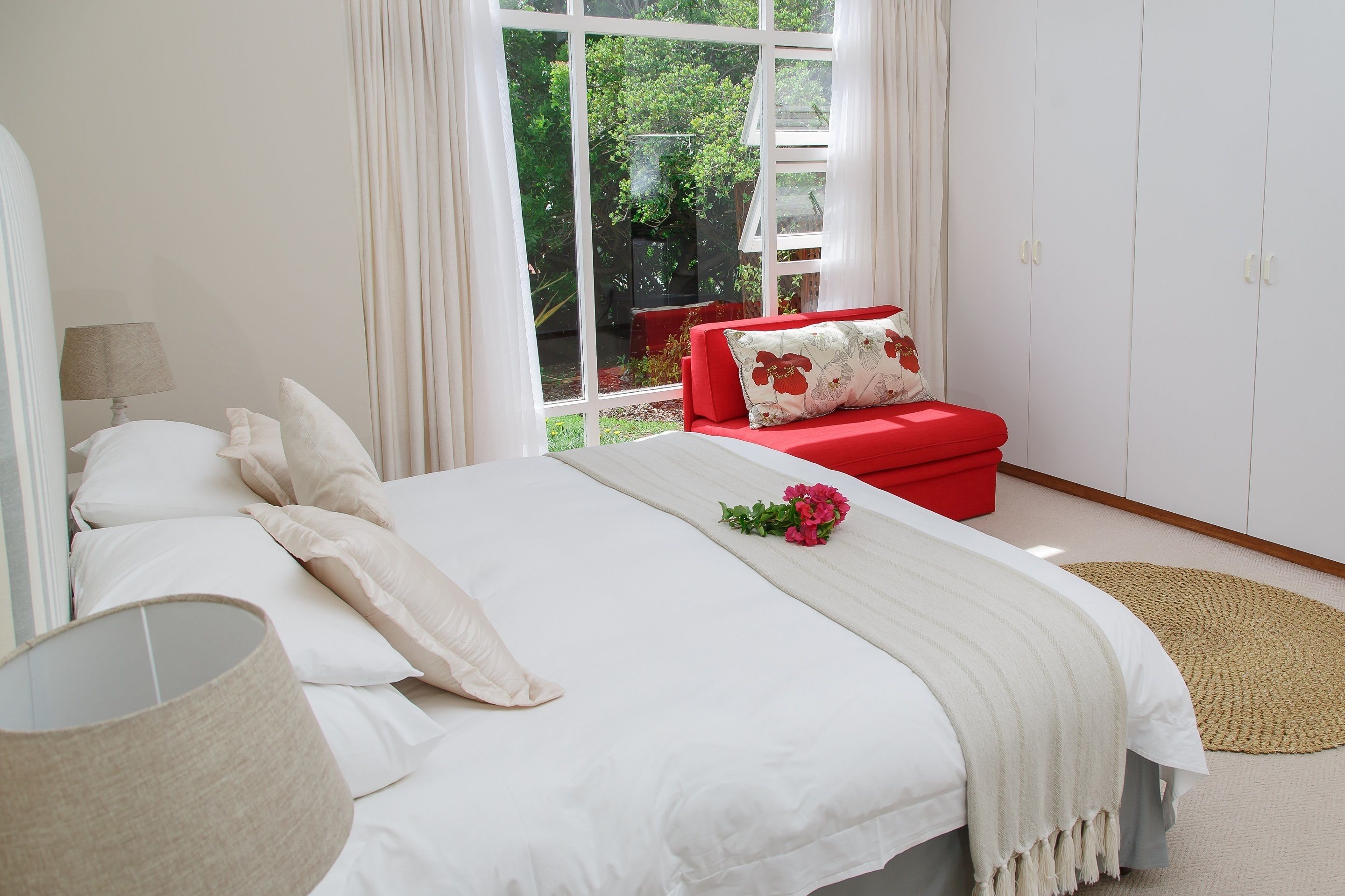 A bedroom with a bed, a red chair, and a view of greenery outside.