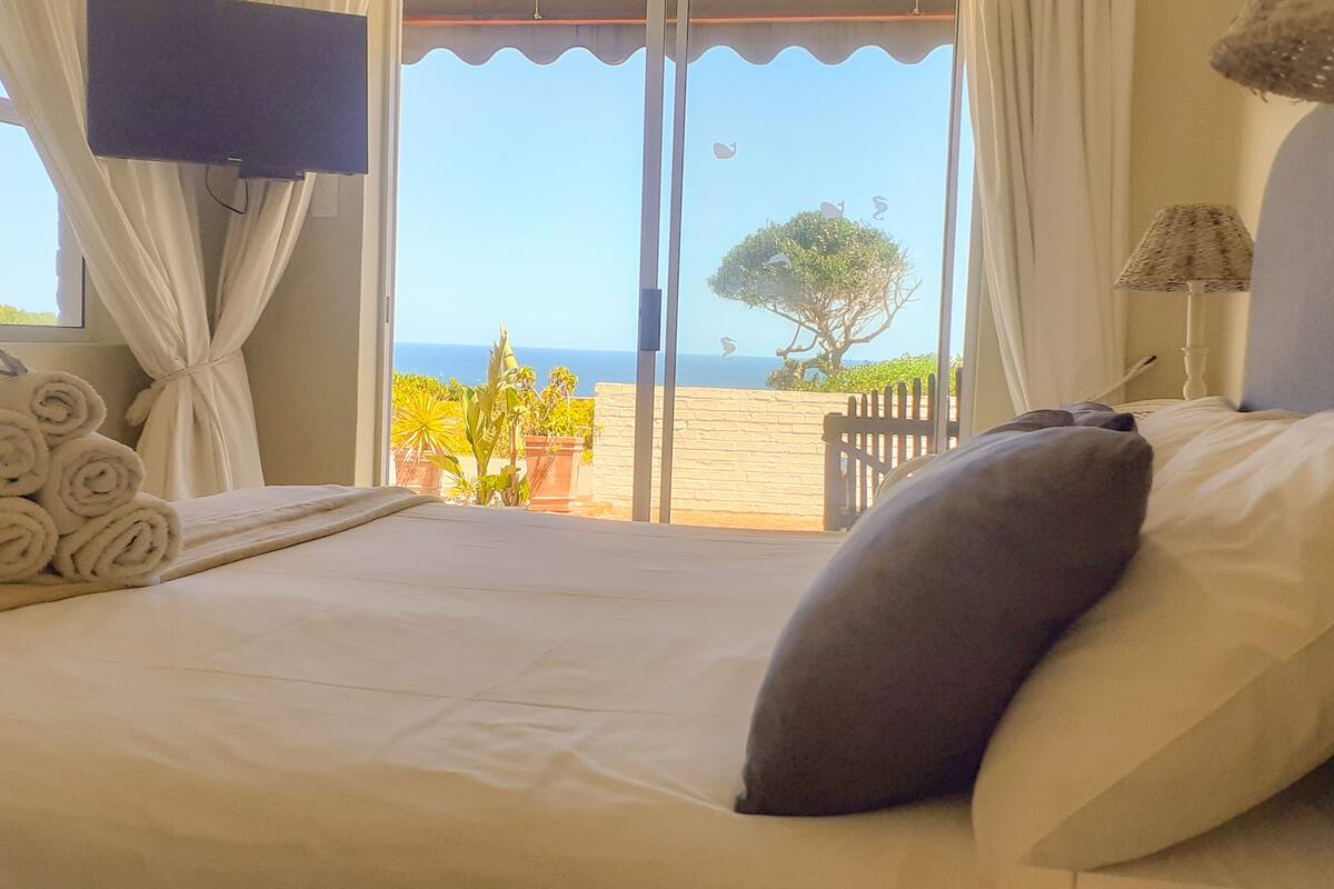Une chambre d’hôtel avec un lit, une vue sur la mer et un balcon agrémenté de plantes.