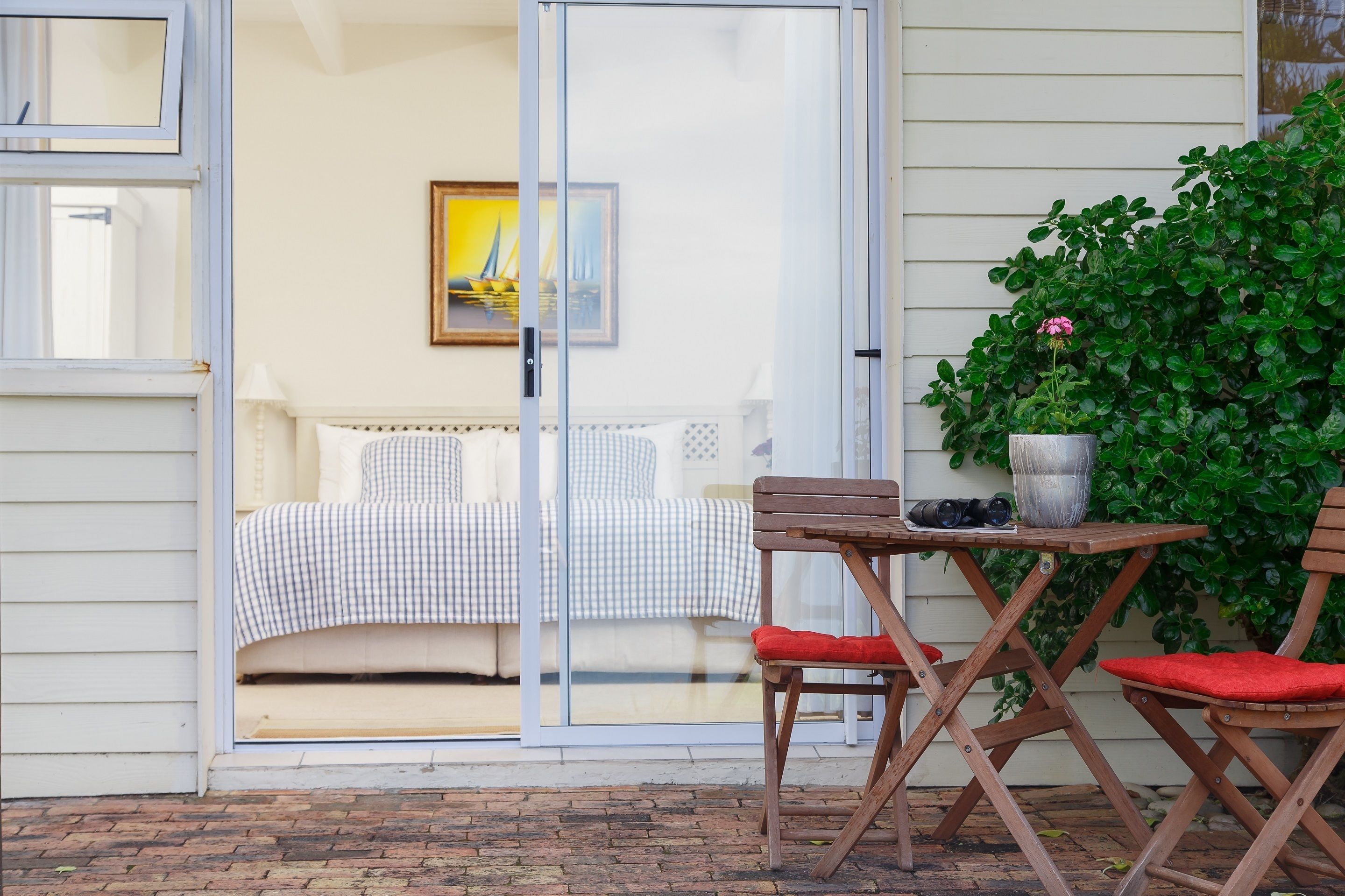 Een slaapkamer met een geruit bedovertrek, een schuifpui die uitkomt op een balkon, en een potplant op het balkon.