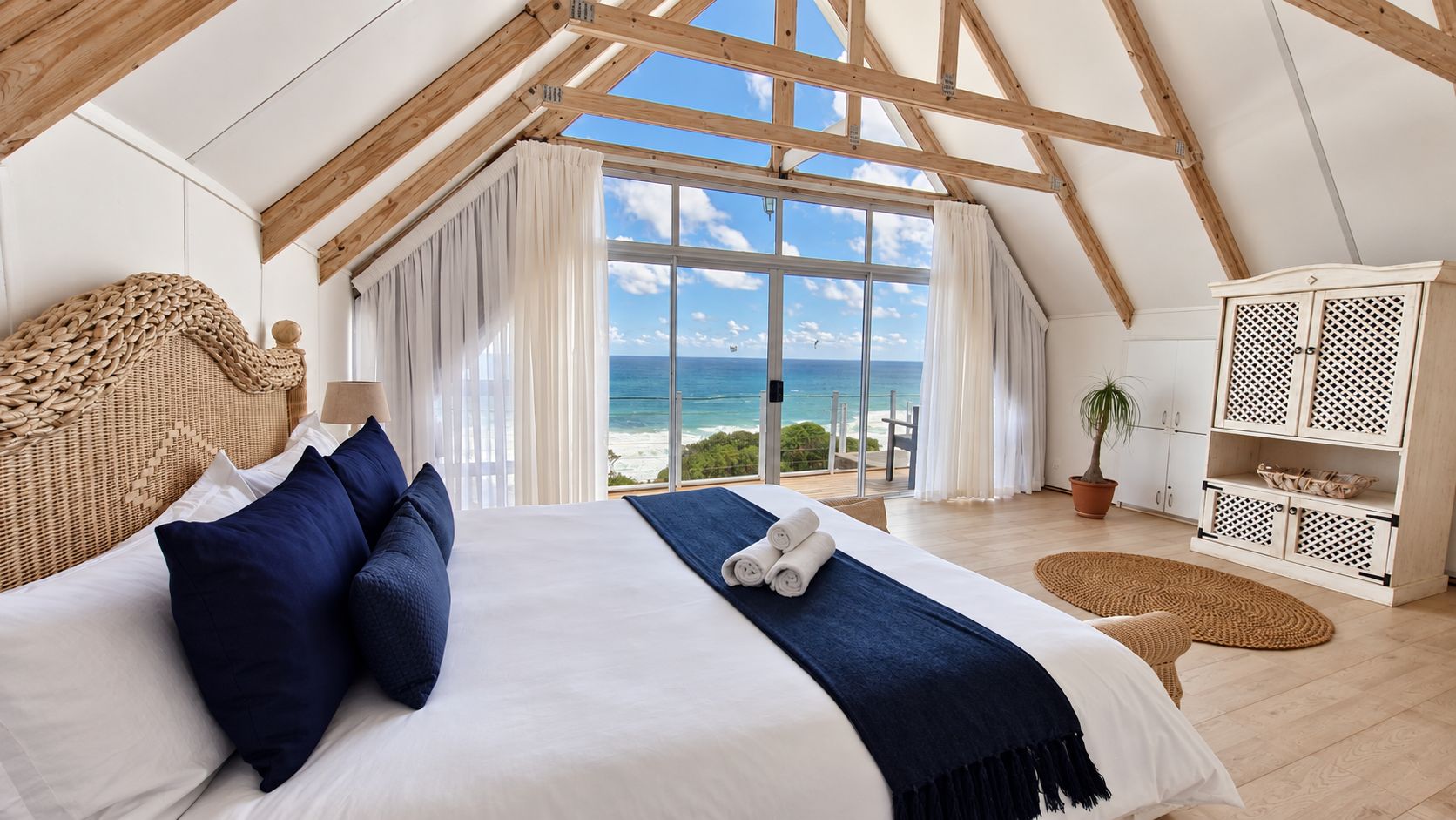 A bedroom with a large bed, a view of the ocean, and a wooden ceiling structure.