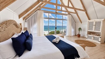 A bedroom with a large bed, a view of the ocean, and a wooden ceiling structure.