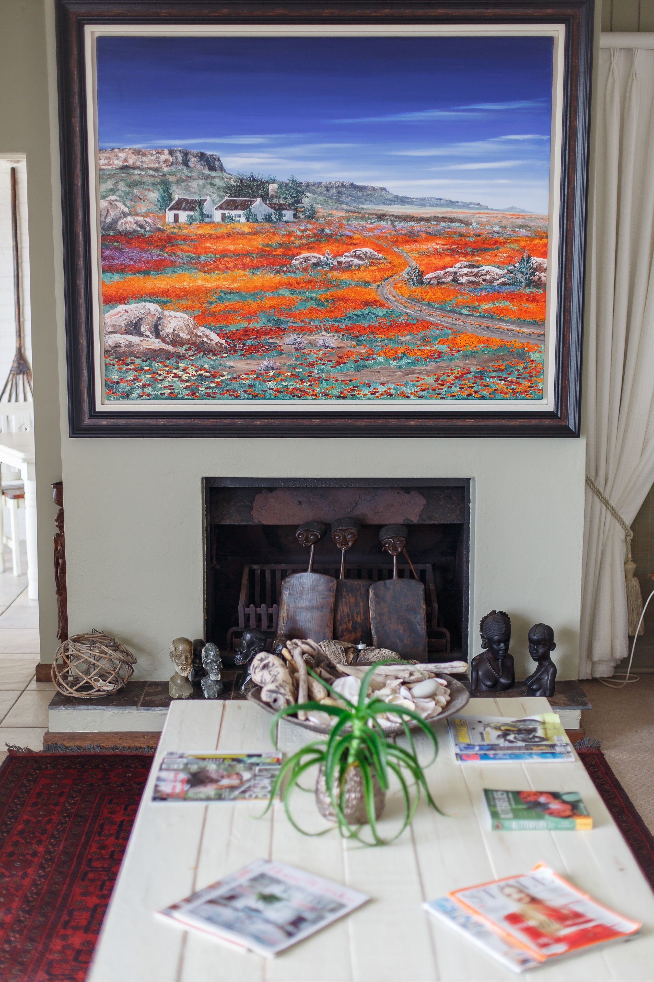 A living room with a large painting above a fireplace, a coffee table with magazines, and a red rug.