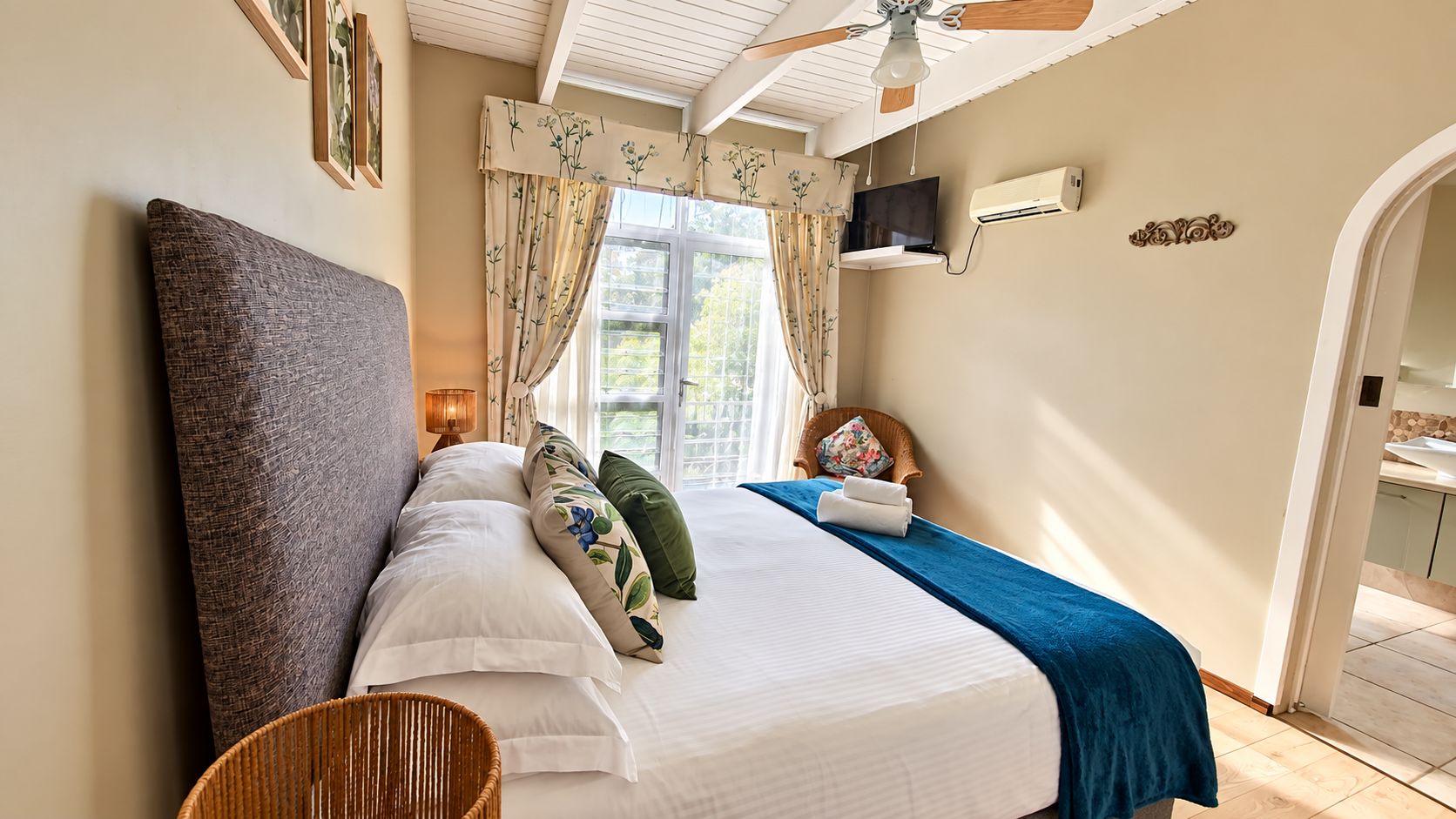 Quarto com cama, travesseiros, mesa de cabeceira, televisão e janela com cortinas.