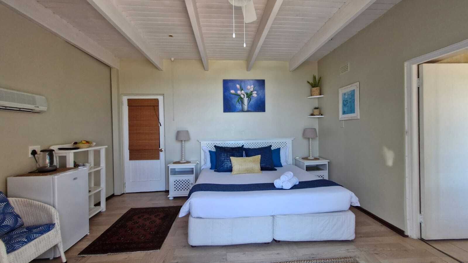 A bedroom with a bed, bedside tables, a chair, a painting, and a door.