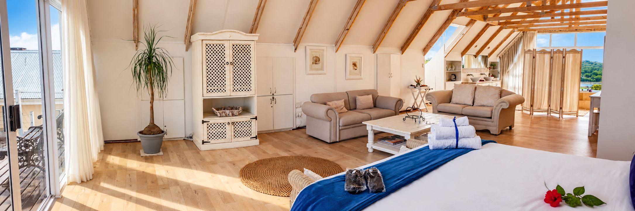 Ein geräumiges Zimmer mit hoher Decke, einem Bett mit blauer Decke, einer Couch, einem kleinen Tisch und einem Schrank mit Gittermuster.