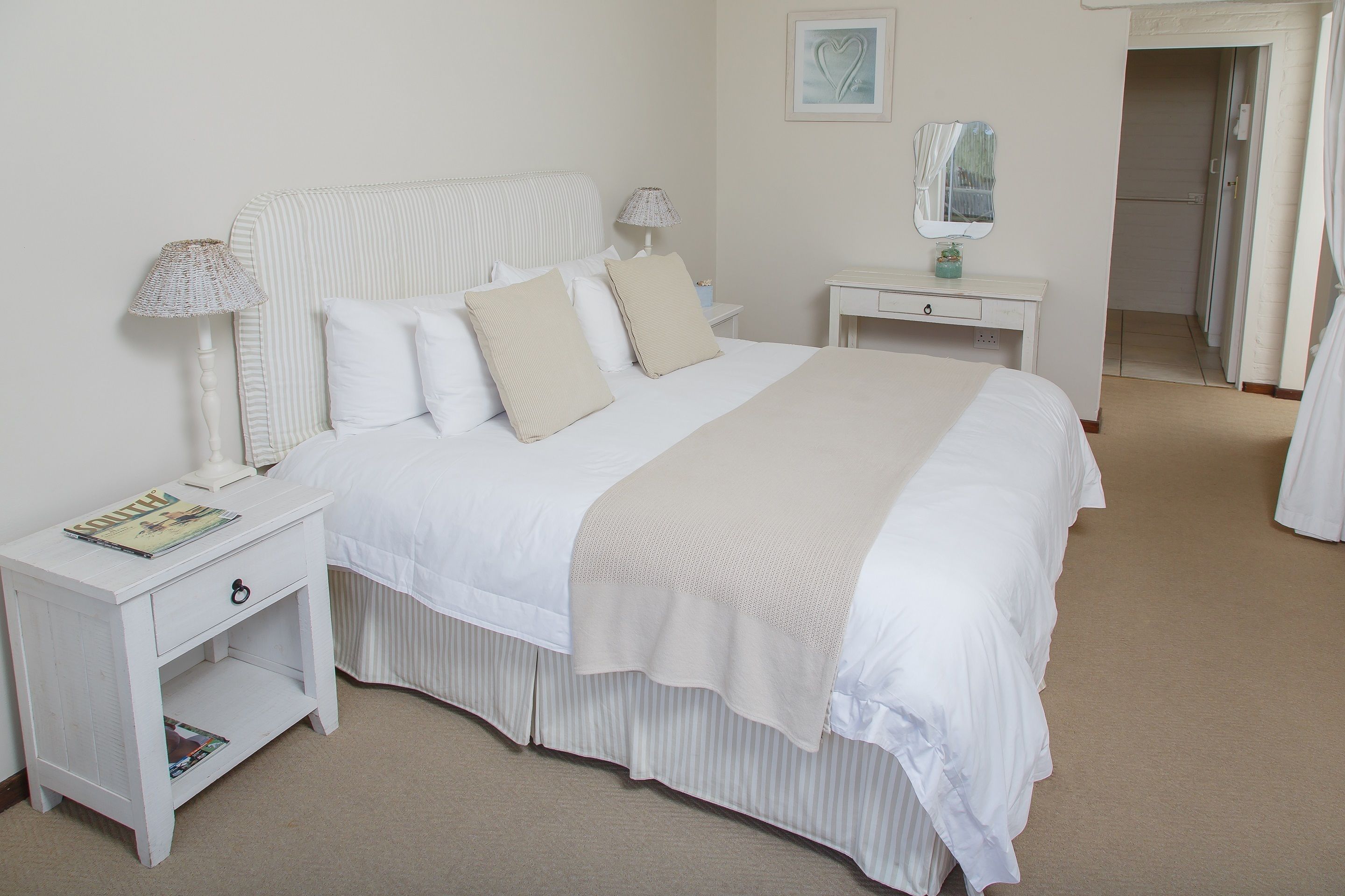 Un dormitorio ordenado con cama, mesitas de noche, cómoda y espejo.