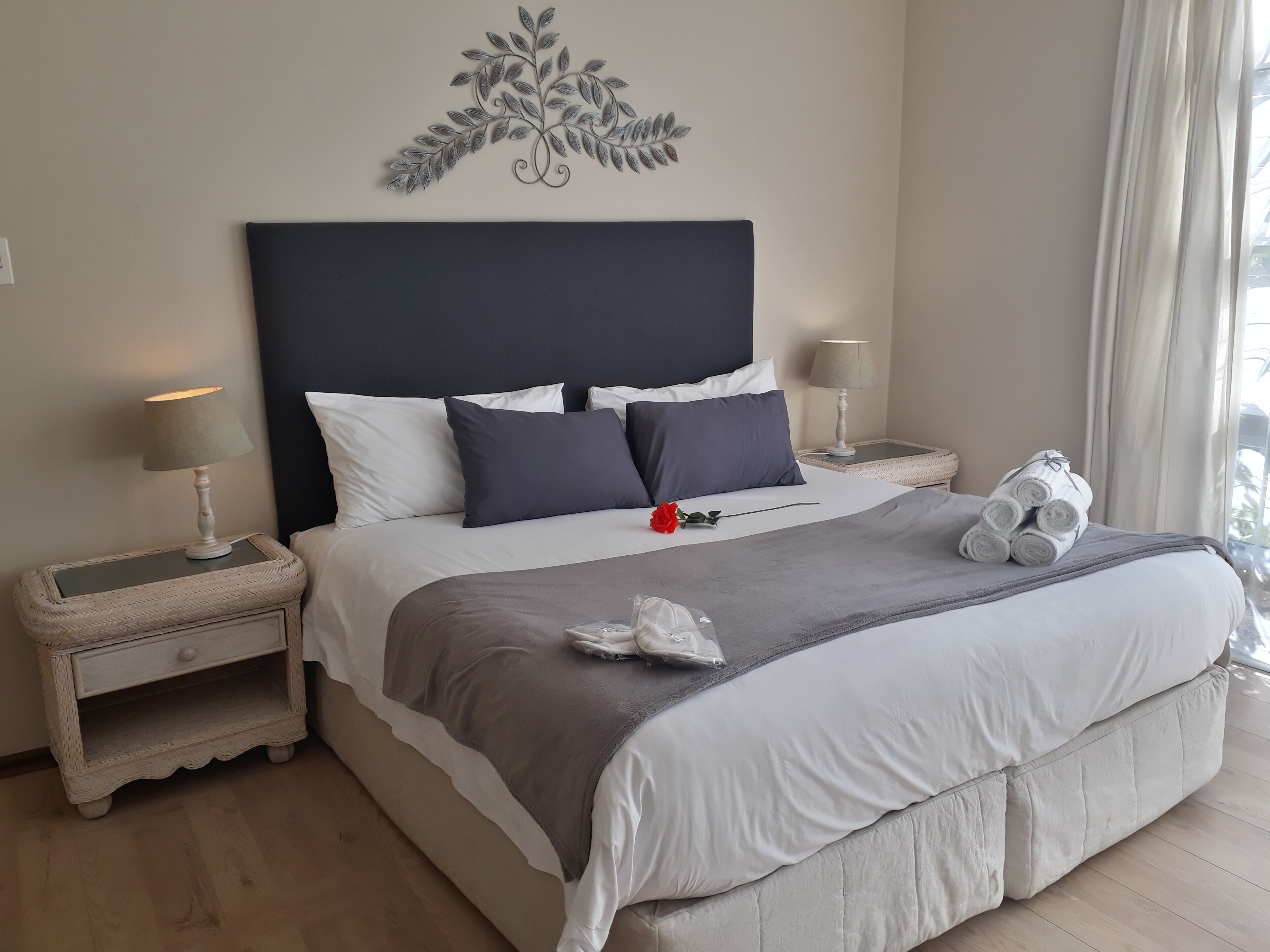 Un lit bien fait, avec une tête de lit sombre, des oreillers blancs et noirs, un plaid gris et un élément décoratif accroché au mur au-dessus.