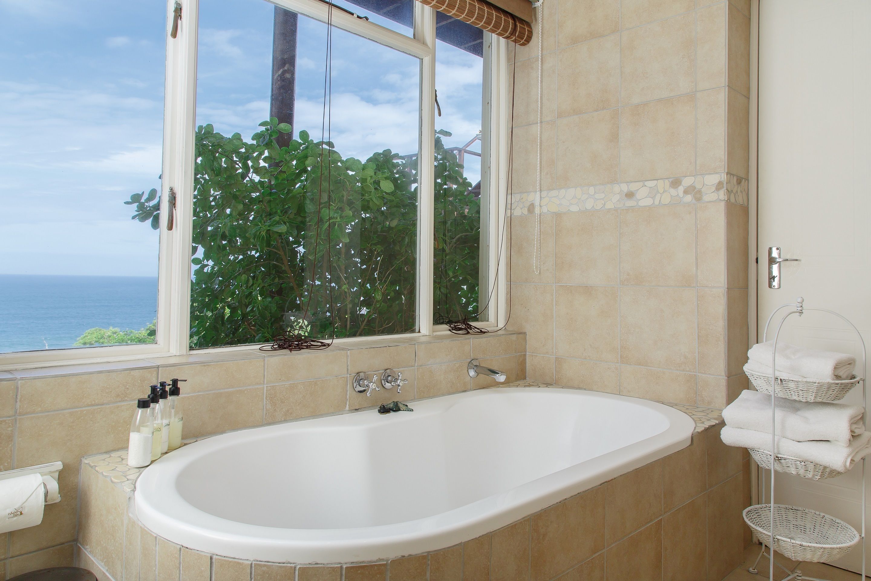 A bathroom with a bathtub, a window with a view of the ocean, and a towel rack with folded towels.